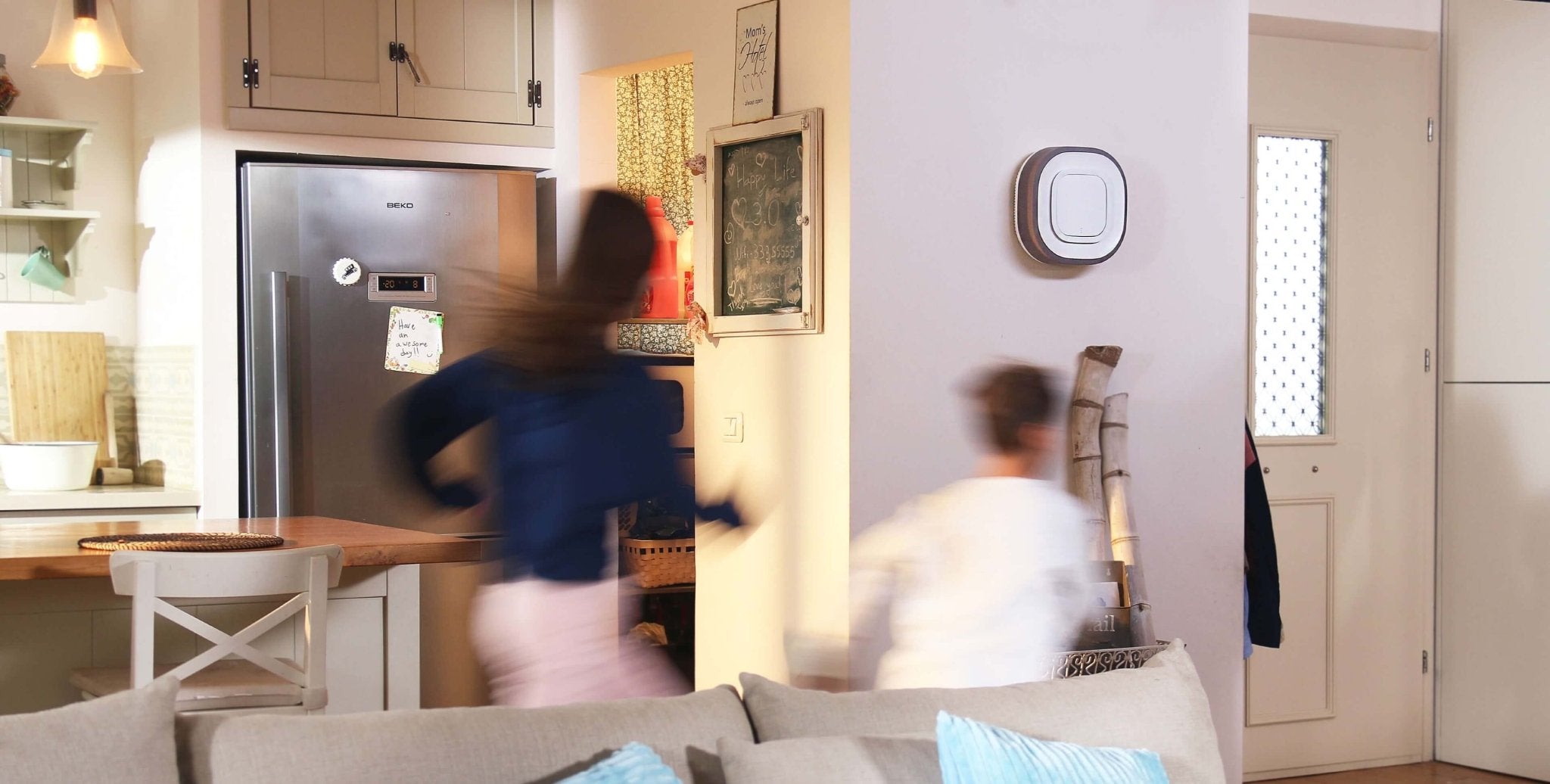 A blurred image of a woman and girl passing an Aura Air Purifier as they exit a kitchen
